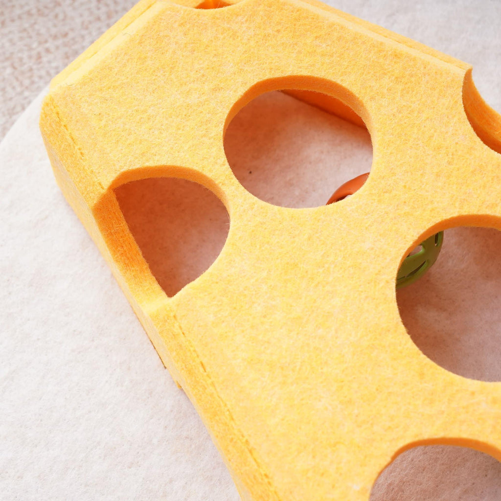 Close-up detail of the yellow felt cheese-shaped cat toy showing its soft texture and round cutout holes with an orange ball visible inside.