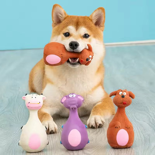 Shiba Inu dog holding an orange latex squeaky toy in its mouth, with three more cute latex animal chew toys (white cow, purple hippo, brown dog) lined up in front.