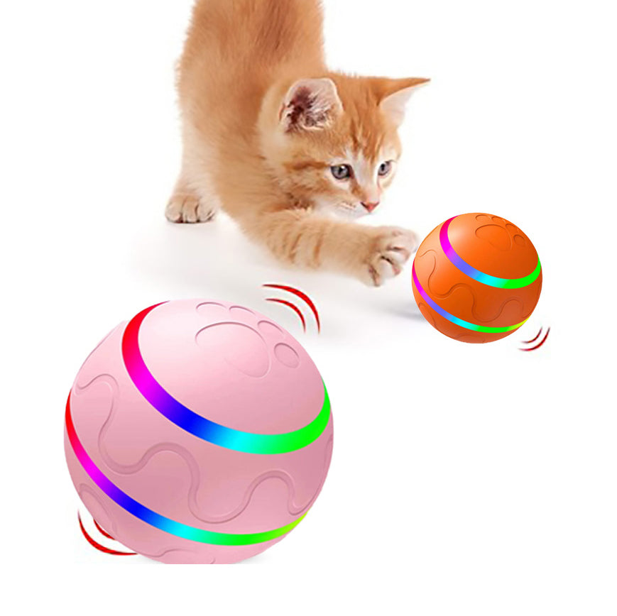Orange kitten reaching for pink and orange intelligent self-rotating cat balls with rainbow LED light strips on white background.