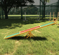 Wooden dog agility seesaw with green anti-slip surface on grass, side view.