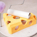 Yellow cheese-shaped felt cat puzzle toy with paper-roll tunnel on top and purple fuzzy ball on a spring wand, on a round base.