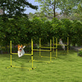 Two dogs jumping through yellow agility jump bars on green grass