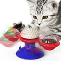 Silver tabby kitten playing with a red windmill cat toy with a blue suction-cup base, white spiky ball, and clear dome with a red ball inside.